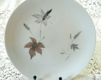 Op de afbeelding: Witte keramische dinerbord met een delicaat bloemenontwerp met bruine, grijze en witte bladeren en stelen.
