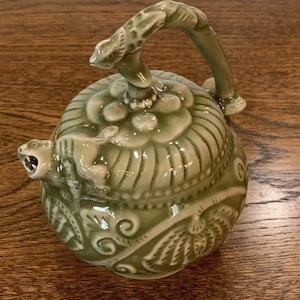 Może przedstawiać: Zielony ceramiczny czajnik z bogatym wzorem kwiatowym i wylewką w kształcie smoka. Czajnik ma unikalny uchwyt w kształcie zakręconego gałęzi.