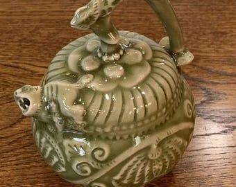 以下が含まれることがあります： 緑色の陶器製のティーポットで、花柄が細かく描かれており、注ぎ口は龍の形をしています。ティーポットは、丸まった枝のようなユニークな取っ手を持っています。