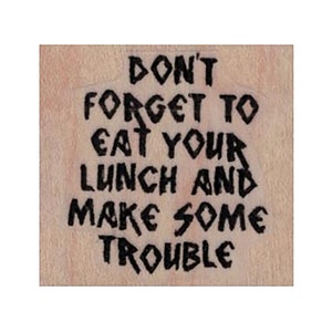 Könnte beinhalten: Ein Stempel aus Holz mit dem Text "Don't forget to eat your lunch and make some trouble" in einer schwarzen, gezackten Schrift.