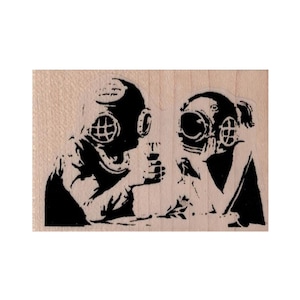May include: Black and white rubber stamp featuring two people wearing diving helmets. The people are facing each other and appear to be talking.