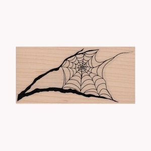 May include: A black and white woodblock stamp with a design of a spider web on a branch.