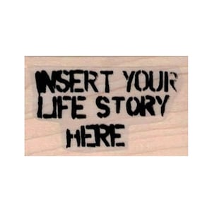 May include: A wooden rubber stamp with the text "Insert Your Life Story Here" in black ink.