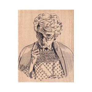 May include: A black and white illustration of an older woman wearing glasses, a patterned top, and a shawl. The woman is pointing her finger and appears to be stern. The image is printed on a wooden block.