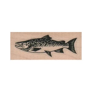 May include: A rectangular wooden rubber stamp featuring a black ink illustration of a fish. The fish is depicted in profile, facing left, with detailed scales, fins, and a visible mouth. The stamp is mounted on a light brown wood block.