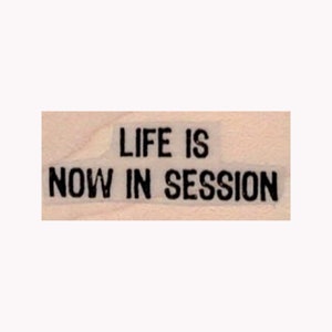 May include: A wooden sign with the text "LIFE IS NOW IN SESSION" printed in black.
