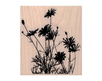 May include: A black silhouette of wildflowers and foliage is stamped on a light wood block. The image features several daisy-like flowers with detailed petals and stems, along with blades of grass. The design is simple and elegant.