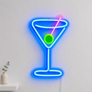 May include: A neon sign shaped like a martini glass with a blue outline, a pink straw, and a bright green olive in the center. The light emits a vibrant glow against the wall, creating a clear silhouette of a cocktail glass with a stem and base.