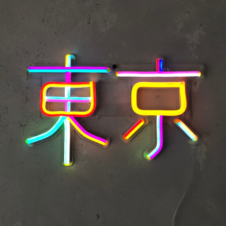 May include: Neon sign with the word "Tokyo" in Japanese characters. The sign is made of multi-colored neon tubes, including pink, yellow, blue, and green.