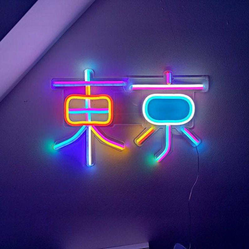 May include: Neon sign with the word "Tokyo" in Japanese characters. The sign is made of pink, blue, yellow, and white neon tubing.