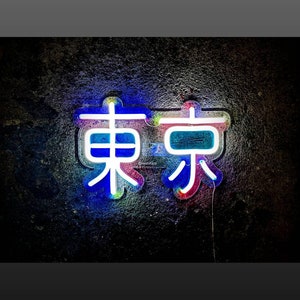 May include: Neon sign with the word "Tokyo" in Japanese characters. The sign is outlined in white and has a blue, pink, and green glow.