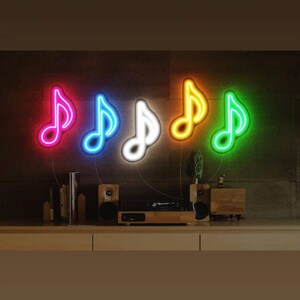 May include: Five neon music note signs in different colors, including pink, blue, white, orange, and green, are mounted on a wall. The signs are lit up and create a vibrant display.