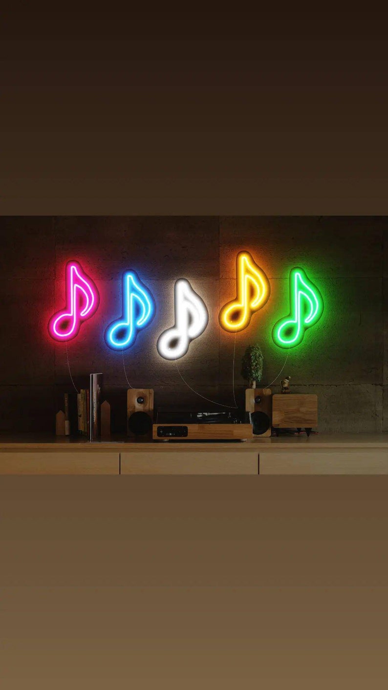 May include: Five neon music note signs in different colors, including pink, blue, white, orange, and green, are mounted on a wall. The signs are lit up and create a vibrant display.