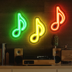 May include: Three neon music note signs on a brick wall. The signs are green, yellow, and orange. There is a record player and speakers on a wooden shelf below the signs.