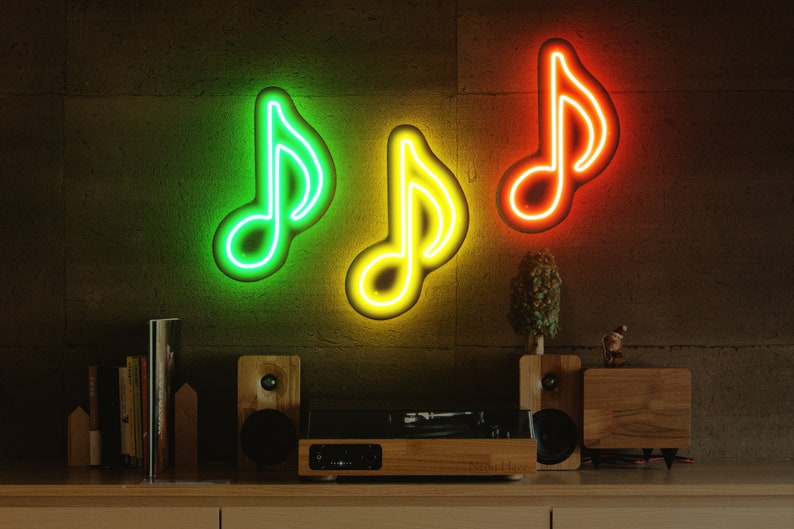 May include: Three neon music note signs on a brick wall. The signs are green, yellow, and orange. There is a record player and speakers on a wooden shelf below the signs.