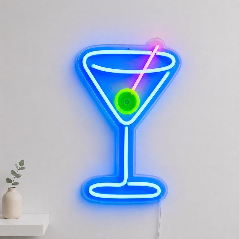 May include: A neon sign shaped like a martini glass with a blue outline, a pink straw, and a bright green olive in the center. The light emits a vibrant glow against the wall, creating a clear silhouette of a cocktail glass with a stem and base.