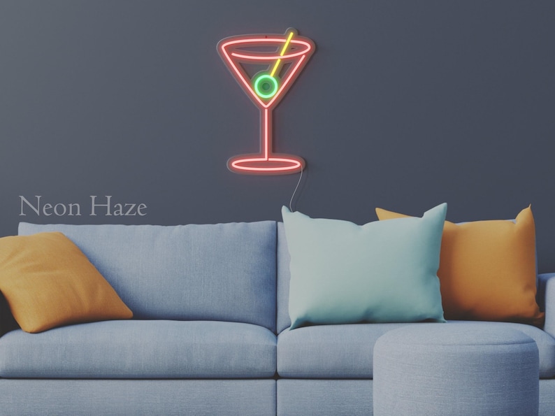 May include: A wall-mounted neon sign shaped like a martini glass with a red outline, a yellow toothpick, and a green olive. The sign features the text Neon Haze in the lower left corner. The light emits a vibrant glow against the dark wall.