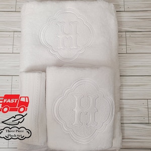 May include: Three white plush towels with an embroidered letter "H" in a decorative circle design. The towels are arranged in a stack, with the largest towel on the bottom and the smallest towel on top.
