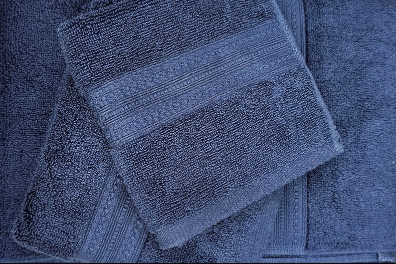 May include: Three blue bath towels folded on top of each other. The top towel has a decorative border.