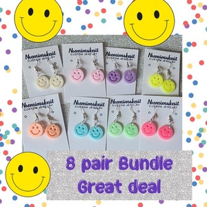 May include: Eight pairs of smiley face earrings in various pastel colors, including white, pink, purple, yellow, orange, blue, green, and light green. The earrings are displayed on white cards with the text "Noemimakesit CUSTOM JEWELRY" on each card. The text "8 pair Bundle Great deal" is displayed at the bottom of the image.