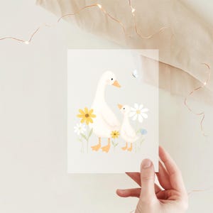 Könnte beinhalten: Eine Grußkarte mit einer Aquarellillustration einer Gänsemutter und eines Gössels, umgeben von gelben und weißen Blumen. Die Gänse sind weiß mit orangefarbenen Schnäbeln und Füßen. Ein kleiner blauer Schmetterling ist im Hintergrund.