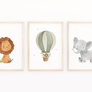 May include: Set of three framed watercolor art prints featuring a lion, an elephant, and a hot air balloon. The lion has a brown mane, the elephant is gray, and the balloon is green and white. The prints are in light wood frames.