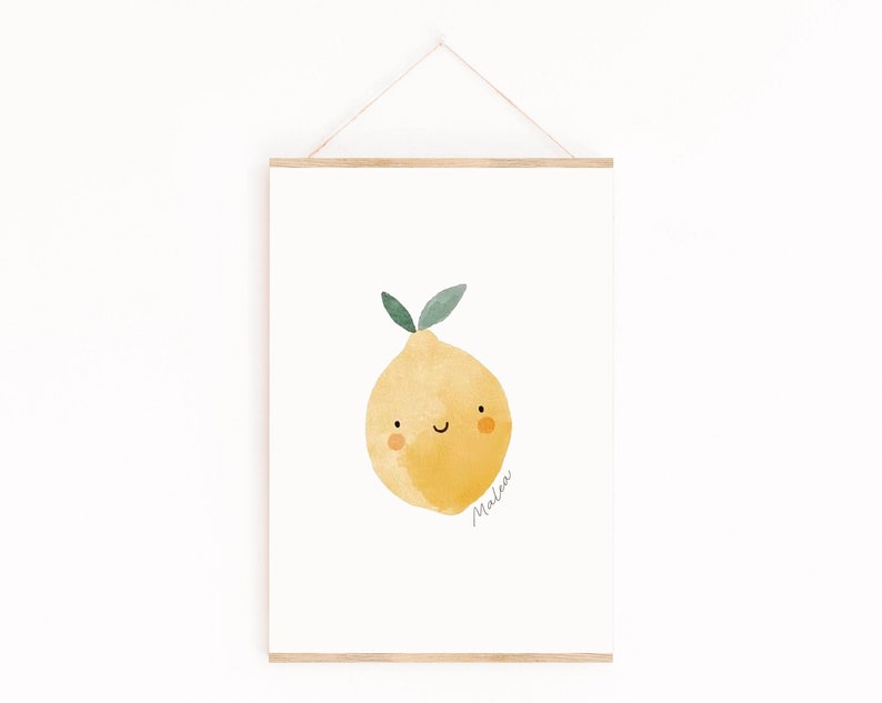 Puede incluir: Una impresi&oacute;n en acuarela de un lim&oacute;n sonriente con hojas verdes. La fruta amarilla tiene una carita feliz y el nombre "Malea" est&aacute; escrito en cursiva. La impresi&oacute;n se muestra en un marco de madera, colgada de una cuerda.