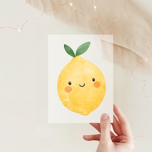 Könnte beinhalten: Eine rechteckige weiße Karte mit einer Aquarellillustration einer leuchtend gelben Zitrone mit lächelndem Gesicht, zwei kleinen schwarzen Augen, rosa Wangen und zwei grünen Blättern oben, vor einem neutralen Hintergrund mit Lichterketten.