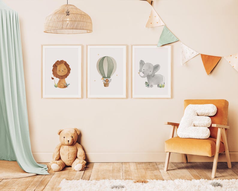 May include: Three framed watercolor prints featuring a lion, hot air balloon, and elephant. The lion is tan with a brown mane, the balloon is green and white, and the elephant is gray. The prints are displayed in a child's room with a teddy bear and a yellow chair.