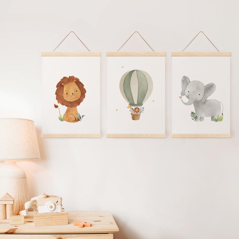 May include: Three framed watercolor prints featuring a lion, a hot air balloon, and an elephant. The lion has a brown mane and sits on green grass. The hot air balloon is green and white. The elephant is gray and has a flower in its trunk.
