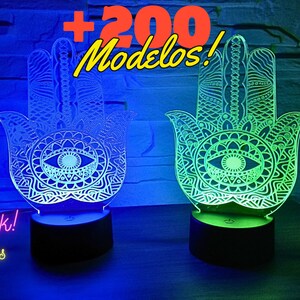 Puede incluir: Dos lámparas de acrílico con forma de mano de Hamsa con un ojo en el centro. Las lámparas están iluminadas en azul y verde. El texto "Mega Pack! Lamparas acrilicas" y "+200 Modelos!" es visible en la imagen.