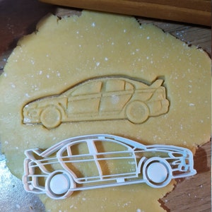 Könnte beinhalten: Ein weißer Plastik-Ausstecher in Form eines Autos. Der Ausstecher liegt auf einem Blatt ungebackenem Keksteig.
