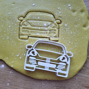 Pode incluir: Cortador de biscoitos de plástico branco em forma da frente de um carro. O cortador está sobre uma superfície amarela com pó branco.