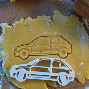 Könnte beinhalten: Ein weißer Plastik-Ausstecher in Form eines Autos. Der Ausstecher liegt auf einem gelben Teig, der auf einer Holzoberfläche liegt.