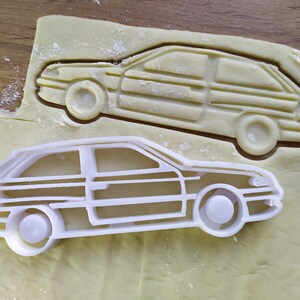 Könnte beinhalten: Zwei weiße Plastik-Ausstecher in Form von Autos. Das größere Auto liegt auf dem kleineren.