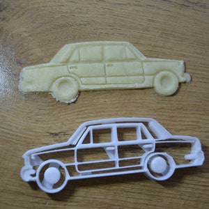 Puede incluir: Un cortador de galletas de plástico blanco con forma de coche antiguo. El cortador de galletas está sobre una superficie de madera.