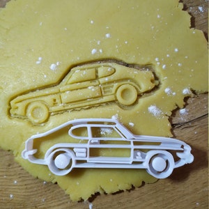 Może przedstawiać: Biała plastikowa foremka do ciasteczek w kształcie klasycznego samochodu Ford Capri. Foremka leży na arkuszu żółtego ciasta do ciasteczek.
