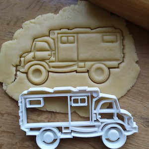 Puede incluir: Cortador de galletas de plástico blanco con forma de autocaravana. El cortador está sobre una superficie de madera con un rodillo y una masa de fondo.