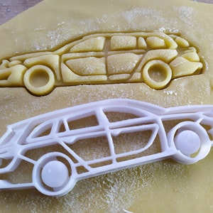 Könnte beinhalten: Ein weißer Plastik-Ausstecher in Form eines Autos. Der Ausstecher liegt auf einer hellbraunen Oberfläche mit einer dunkelbraunen Umrandung der gleichen Autoform.