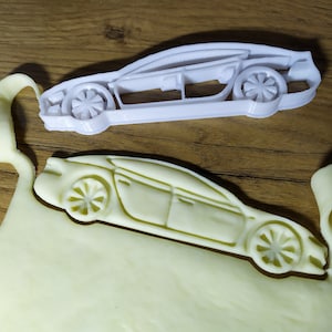 Könnte beinhalten: Ein weißer Plastik-Ausstecher in Form eines Autos. Der Ausstecher liegt auf einem Stück weißen Teigs, der in Form eines Autos ausgeschnitten wurde.