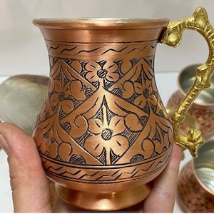 May include: Set of four copper mugs with intricate floral designs and a hammered finish. Each mug has a curved handle and a wide base.