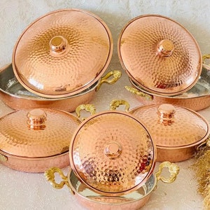 May include: Set of six copper cookware with a hammered finish and handles. The cookware is arranged in a circular pattern on a white surface.
