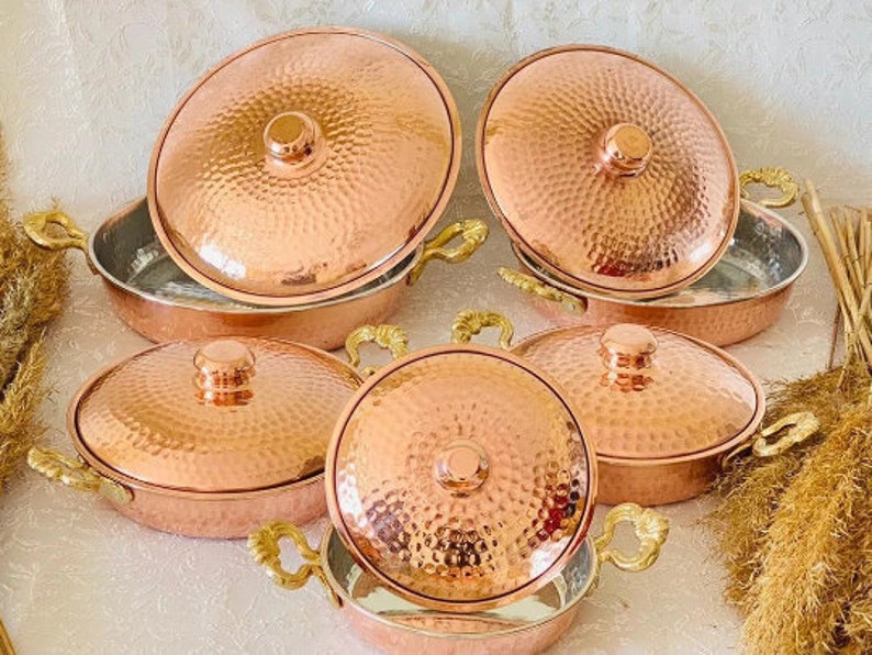 May include: Set of six copper cookware with a hammered finish and handles. The cookware is arranged in a circular pattern on a white surface.