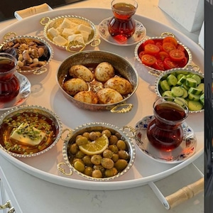 Peut inclure: Un plateau blanc garni de divers plats de nourriture, notamment des œufs, des olives, des tomates et des noix. Plusieurs petits verres de thé sont également présents. Les plats sont dans des bols en métal décoratifs avec des poignées.