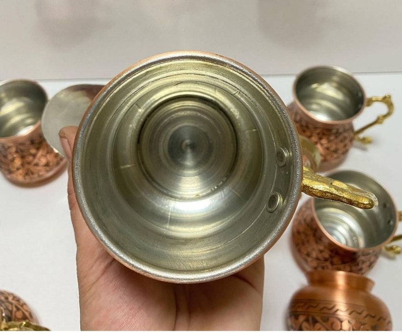 May include: Set of six copper mugs with ornate designs and gold handles. The mugs have a shiny, metallic finish and are perfect for serving beverages.