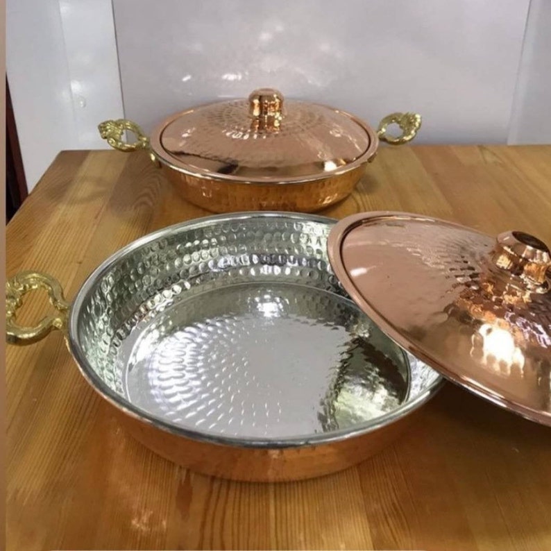 May include: Two copper pots with lids and gold handles. The pots have a hammered finish and are suitable for cooking.