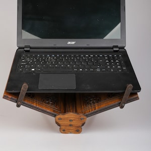 Op de afbeelding: Een zwarte laptop op een donkerhouten standaard. De standaard heeft ingewikkelde houtsnijwerk en is ontworpen om een laptop in een hoek te houden.