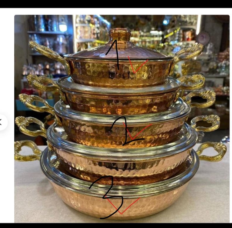May include: A set of five copper pots with hammered finishes and gold-coloured handles. The pots are stacked on top of each other, with the largest pot at the bottom and the smallest pot at the top.