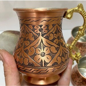 May include: Set of six copper mugs with intricate floral designs and gold handles. The mugs are perfect for serving Turkish coffee or tea.