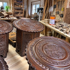 Può includere: Tre tavolini rotondi in legno con finitura marrone scuro e intricati motivi geometrici intagliati a mano sui piani e sui lati. Ogni tavolo presenta un bordo smerlato e una base cilindrica con dettagliati motivi floreali e a stella.